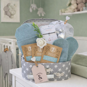 Newborn baby gift box with sage green knit hat and mittens in a grey suitcase with star pattern.