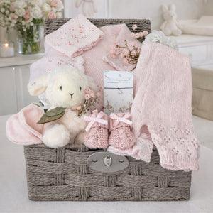 Baby girl hamper basket packed with gifts to welcome a new baby girl with pink knit clothing and a cuddly lamb.