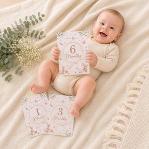 Baby in white dressing gown with a 6 months milestone card. Bumbles and Boo.