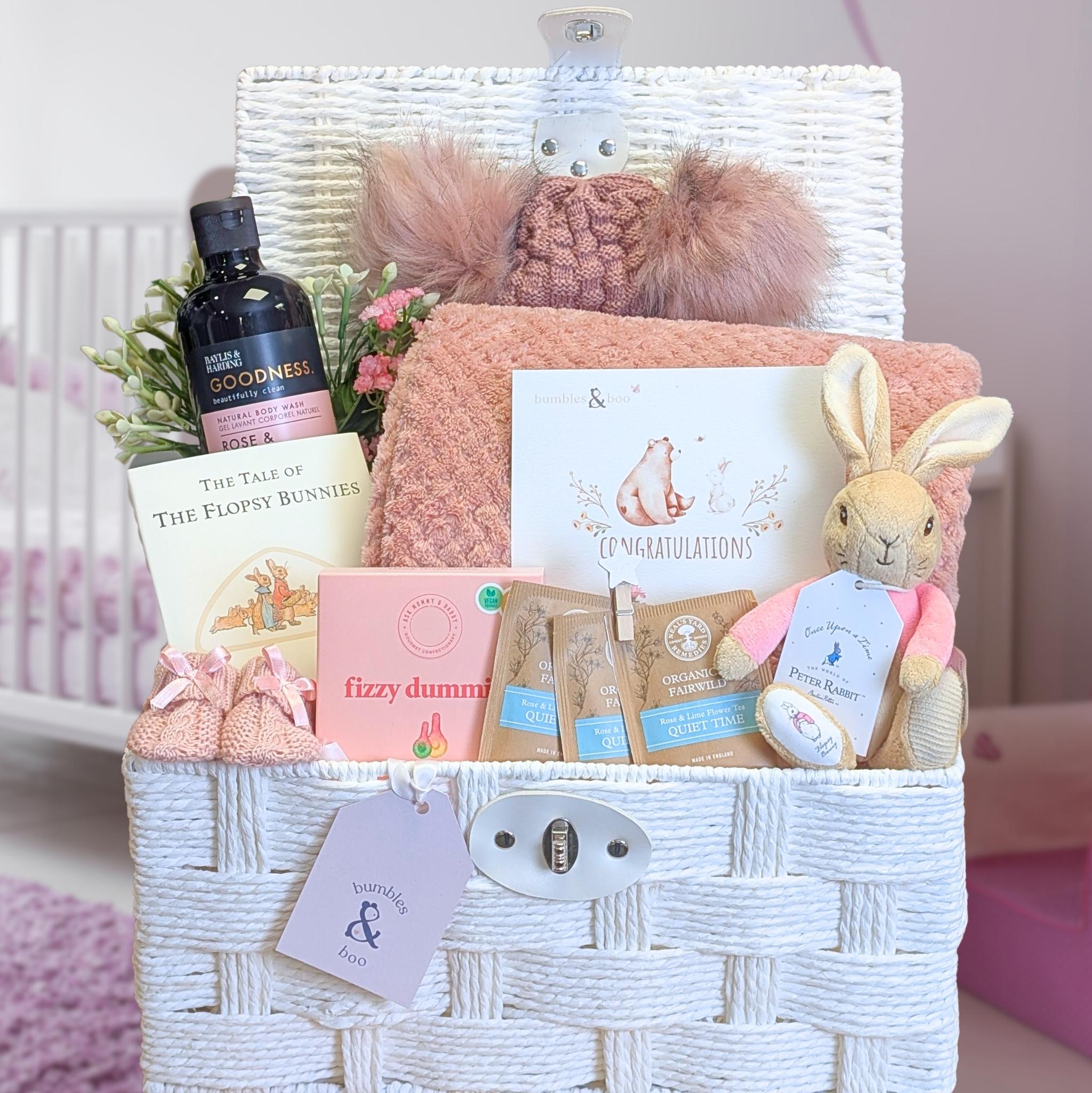 New mum gift hamper basket with presents for her and baby items including a plush toy, book, and blanket in a white basket.