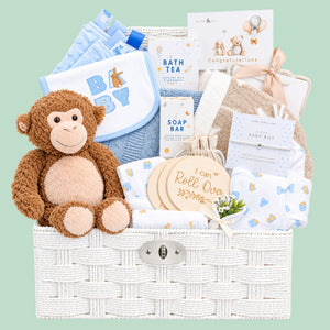 Newborn baby boy gifts in a white hamper basket which includes a steiff monkey soft toy and blue and white clothing set.