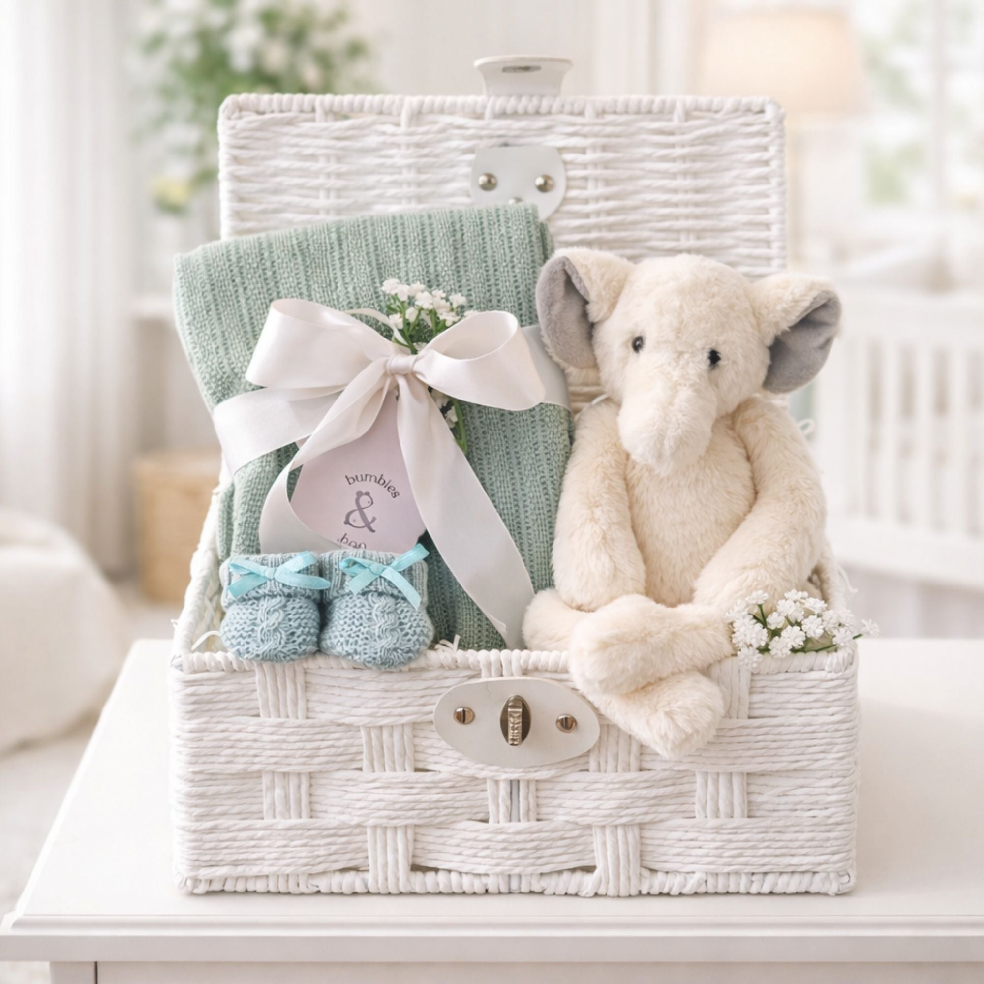 Newborn baby gifts in a white hamper basket with an elephant and green blanket