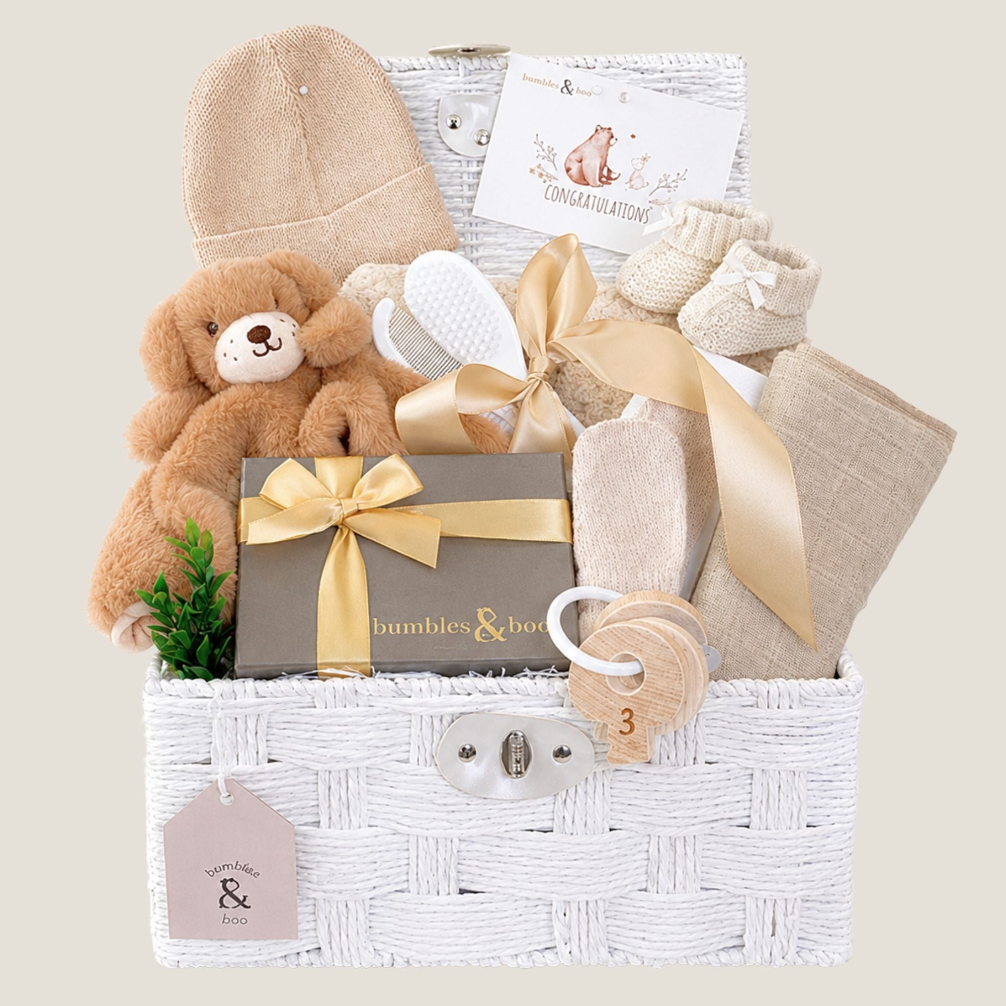 Newborn baby gifts basket with teddy bear, hat, and other items in a white hamper
