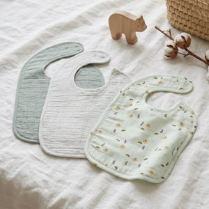 Three rounded baby bibs in vegetable print, pale grey and green
