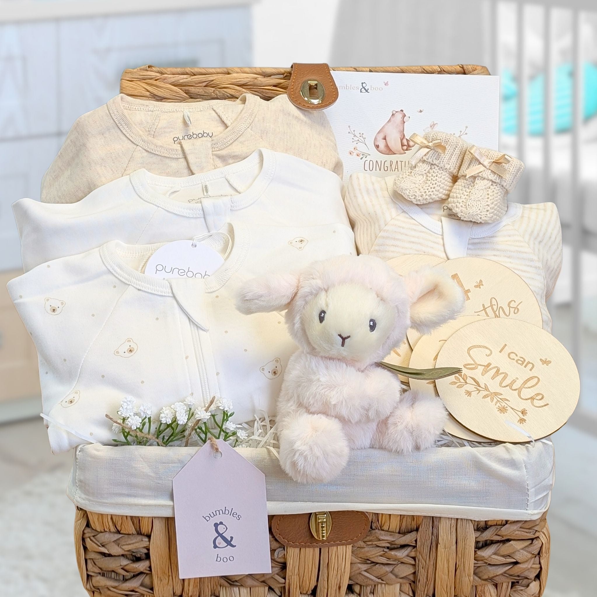 A nursery basket full of organic clothing gifts and a lamb soft toy rattle.
