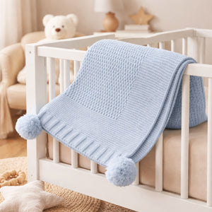 A pale blue baby blanket with pompoms in a knit design.