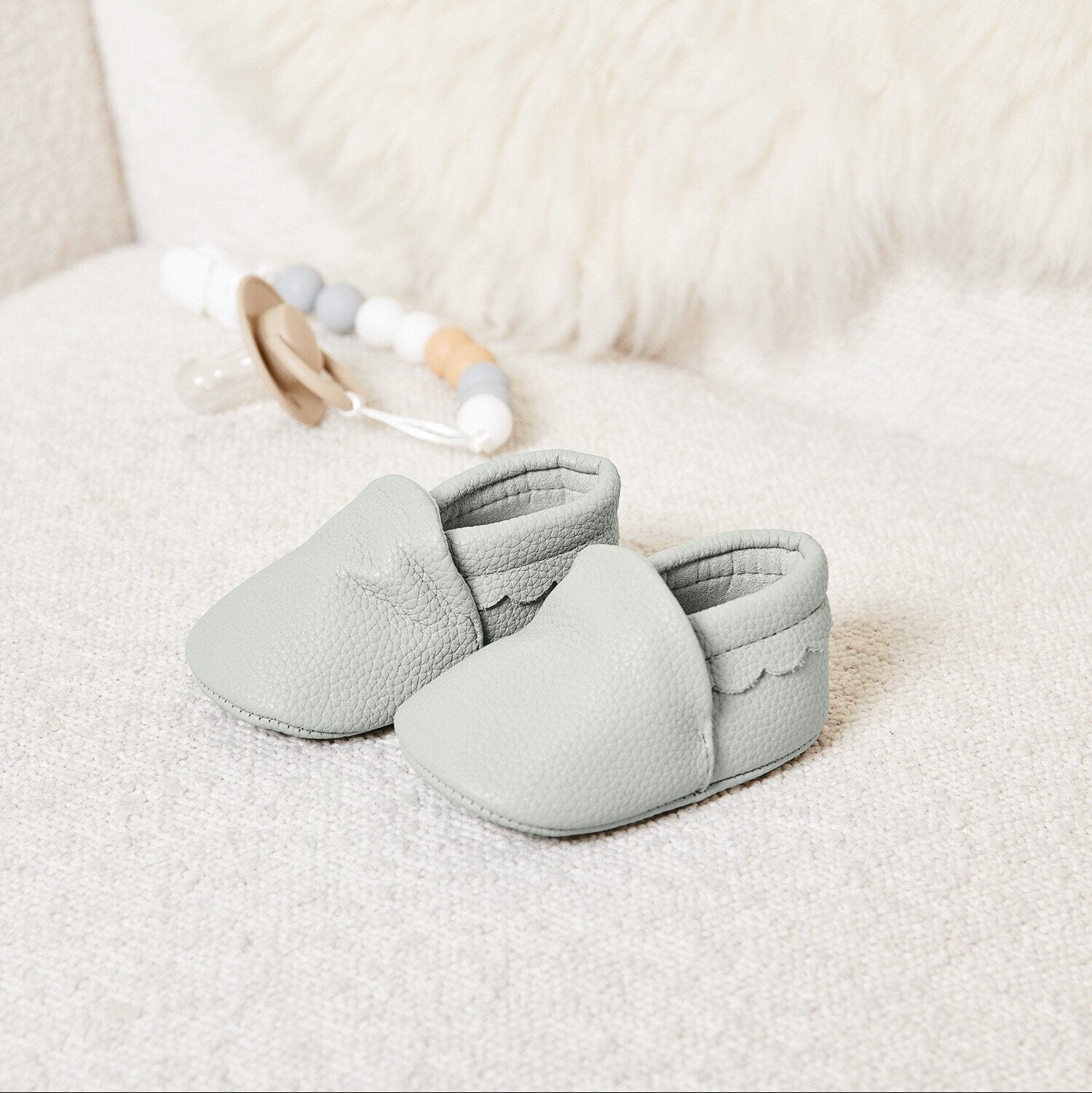 Pair of pale grey baby booties with scalloped trim in soft vegan leather, neutral baby shoes for newborn baby clothes collection.