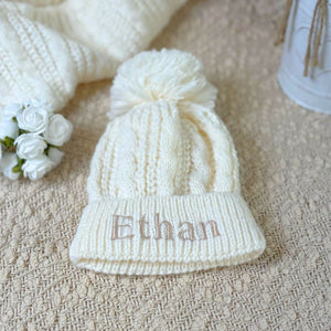Personalised baby hat in a cream pearl and cable knit design with a large pom pom