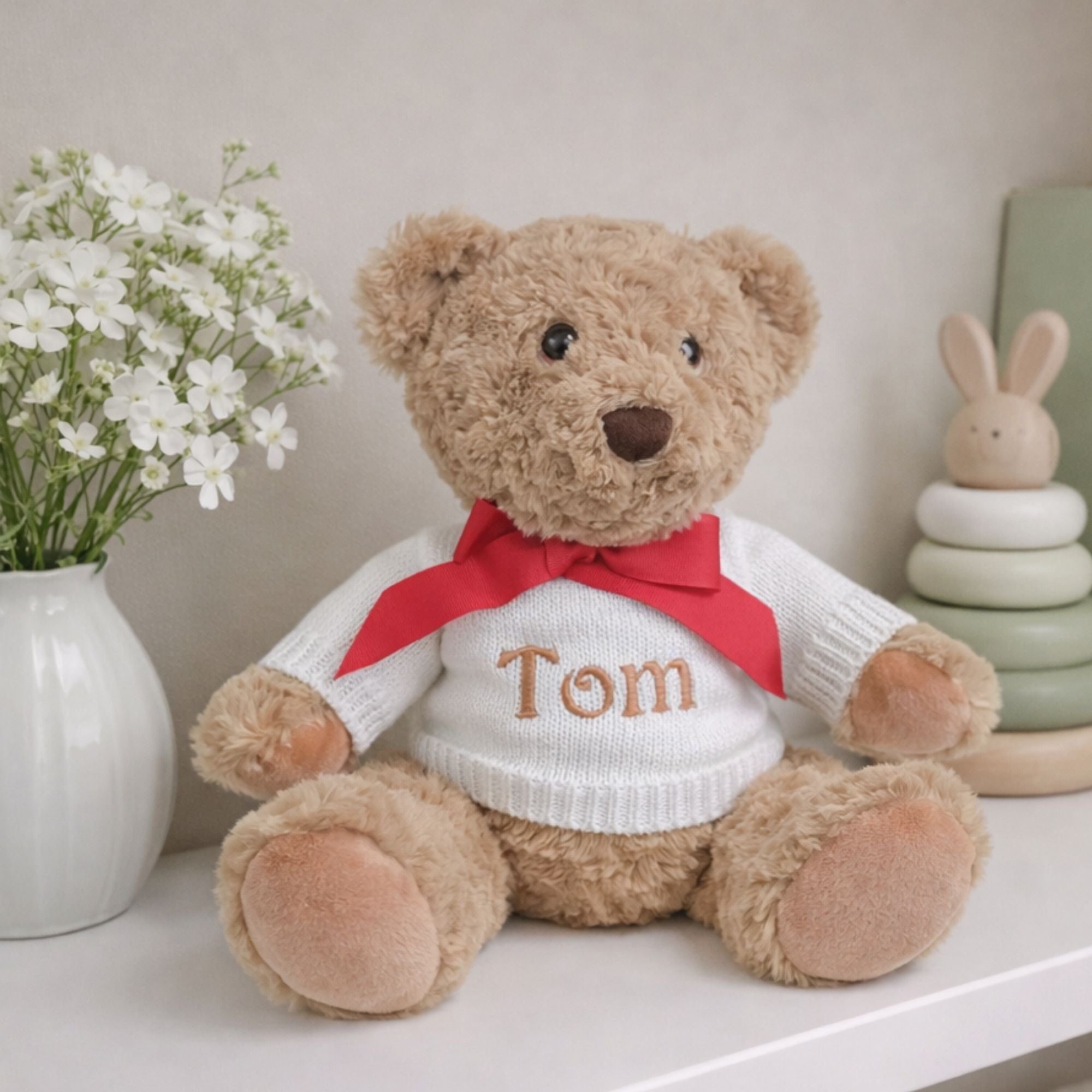 Personalised teddy bear with a red ribbon and white jumper customised with the baby's name in embroidery.