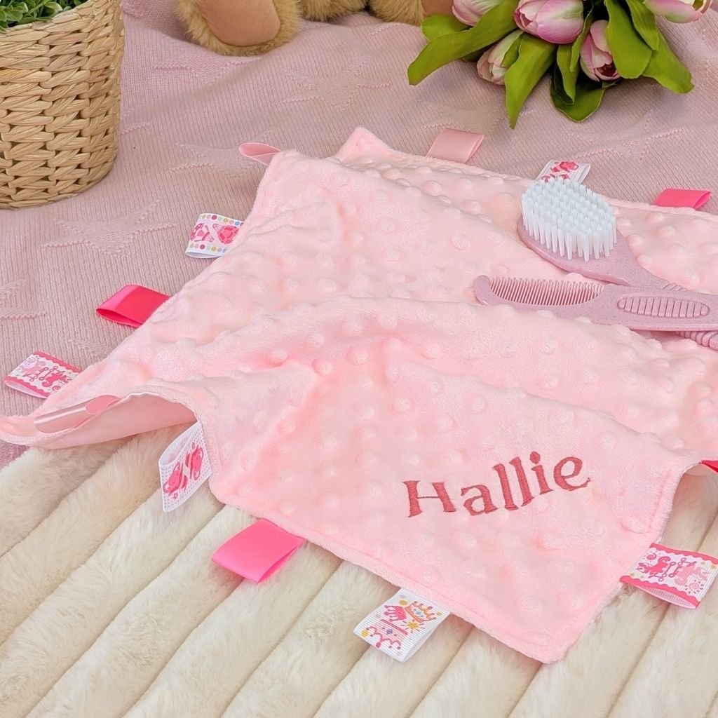 Personalised baby comforter in pale pink with taggie ribbons and the name 'Hallie' embroidered in dark pink