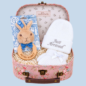 Peter Rabbit new baby hamper in pink floral keepsake suitcase with wooden ring rattle, white Just Arrived knitted baby hat and matching booties.