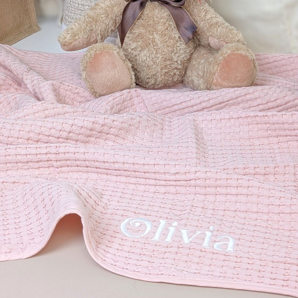 A light pink waffle texture baby blanket with the name 'Olivia' printed on it.