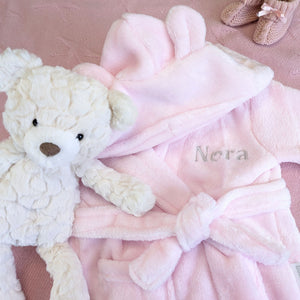 Pink hooded baby dressing gown embroidered with Nora, displayed beside a teddy bear and flowers.