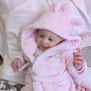 Baby wearing a pink dressing gown with an ear-detail hood and an embroidered name.
