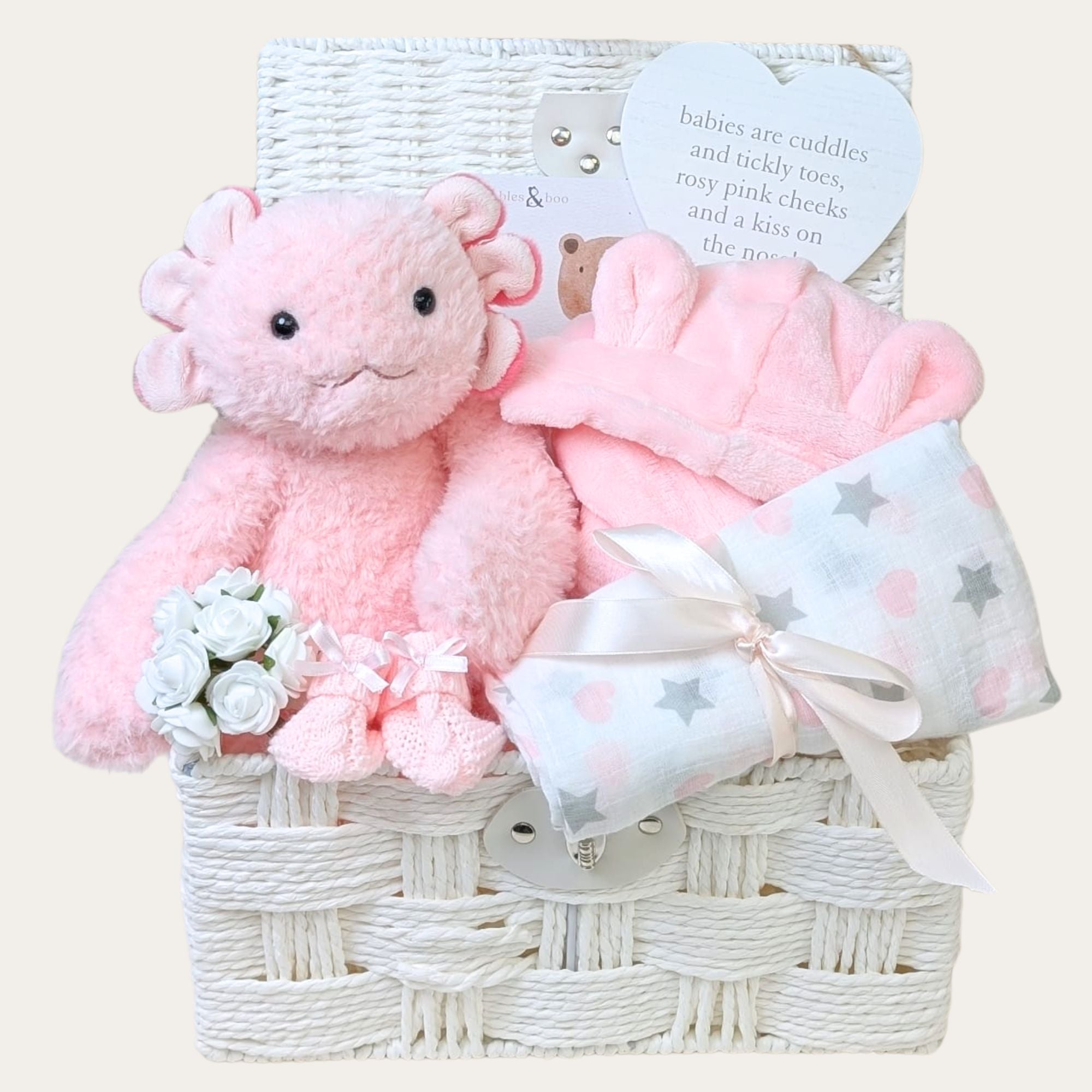 Gifts for a new baby girl in a white hamper basket. Presents include a pink axolotl, designed by Bumbles and Boo.