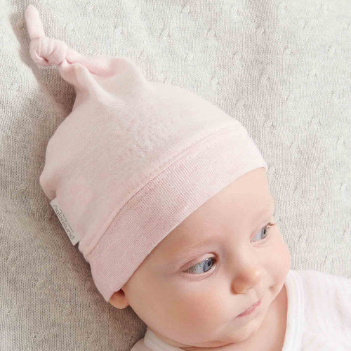 Pink organic cotton baby knot hat with adjustable top knot and ribbed band, soft newborn baby clothes hat in gentle blush fabric.