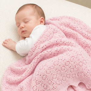 Pink cashmere baby blanket. This shawl has a delicate pointelle openwork pattern and is covering a sleeping newborn baby