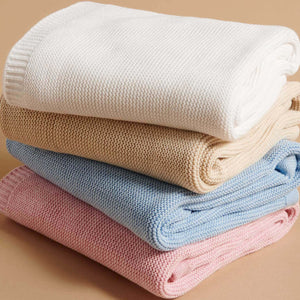 Stack of folded knit blankets in white, beige, blue, and pink . Organic Cotton