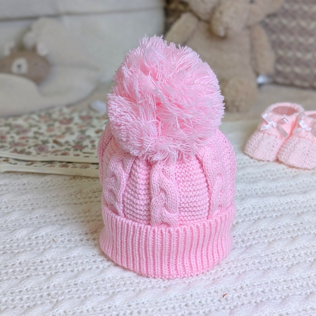 Pink knitted baby hat with a pom-pom.