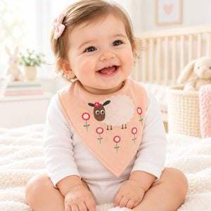 Baby wearing a peach pink bandana bib with a sheep and flower design.