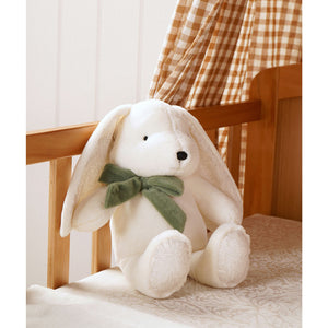 Cream plush bunny with green bow seated on a patterned nursery chair