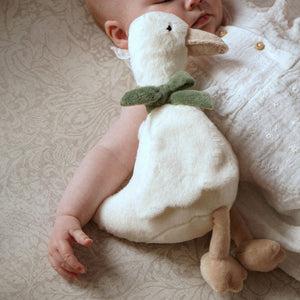 Cream plush goose with green bow resting beside a baby on patterned bedding