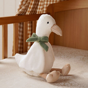 Goose soft toy with long neck and green bow seated on patterned fabric