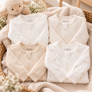 Four folded baby zip-up sleepsuits in soft neutral tones and made with organic cotton