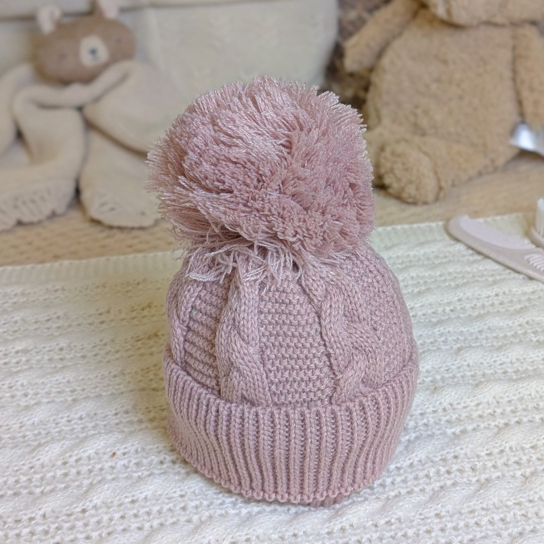 Dusky pink knitted baby hat with a pom-pom.