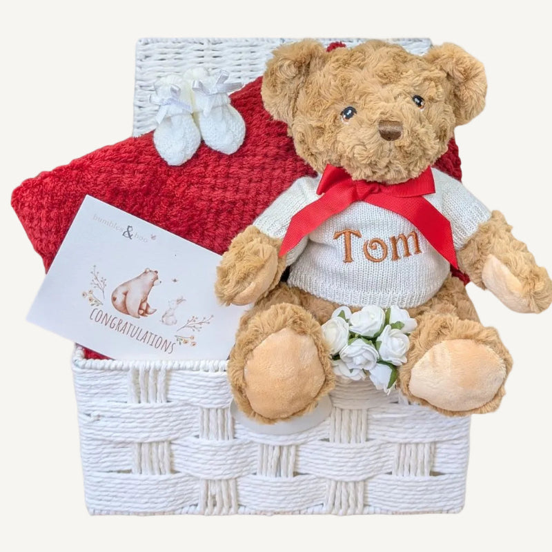 Teddy bear with a sweater and bow tie in a baby gift basket.