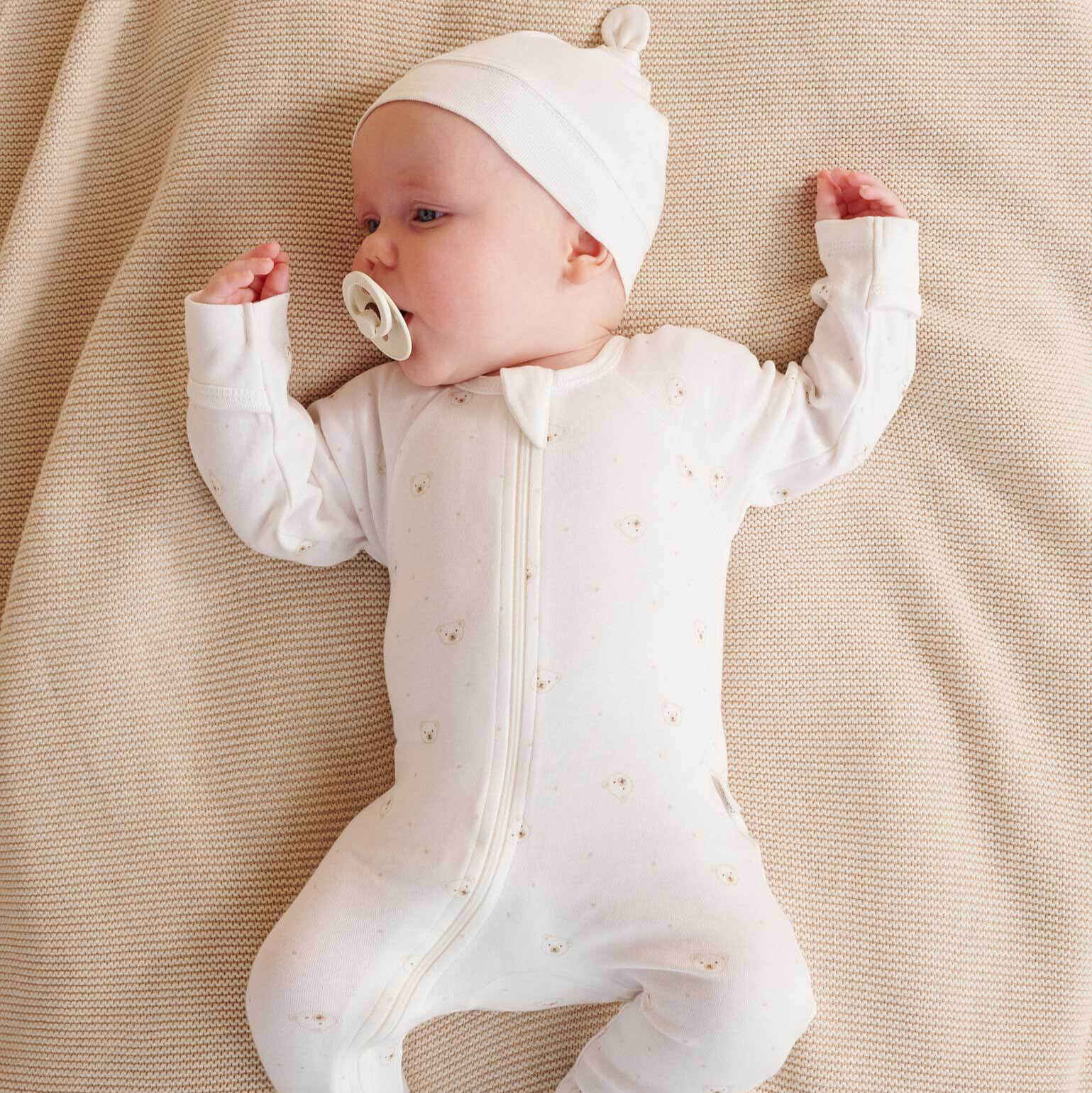 Baby in a white onesie with a hood lying on a beige blanket