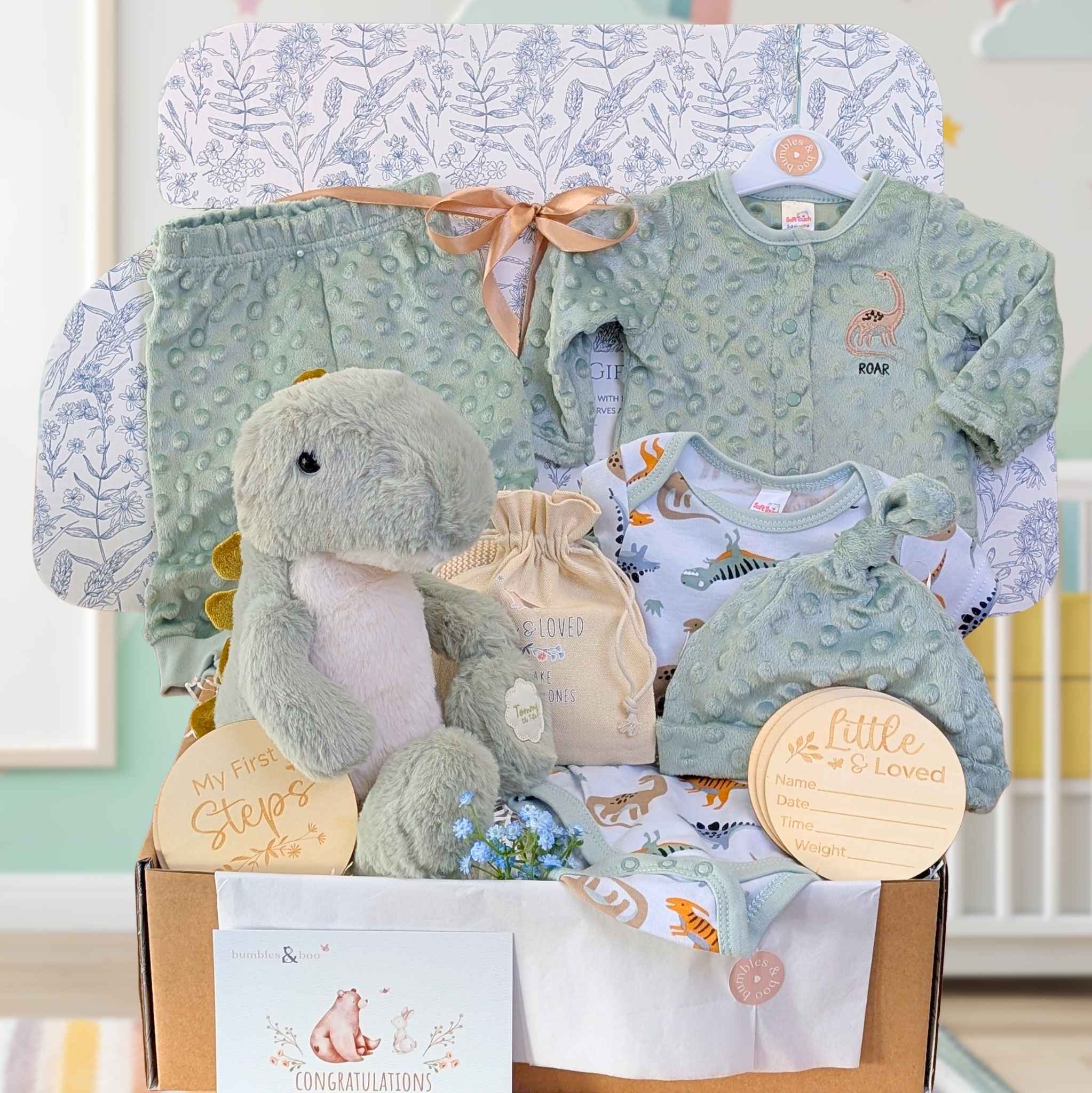 Baby gift box with dinosaur soft toy and sage green clothing in a hamper box.