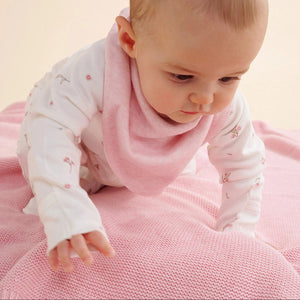 Soft pink organic cotton baby blanket with ribbed trim, and a baby crawling across it