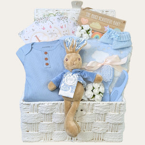 Baby boy hamper basket with gifts including Peter Rabbit, blue blanket and blue sleepsuit.