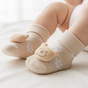Beige baby socks with a teddy rattle on each foot.