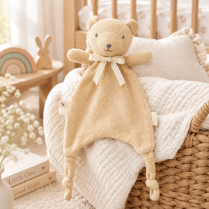 Wheat coloured bear comforter with knotted feet and ribbon tabs resting on a cream blanket