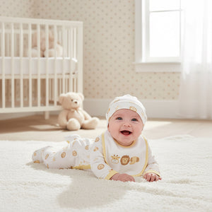 White baby clothes set with yellow safari animal design. Baby wearing the sleepsuit, hat and bib laying on the floor.