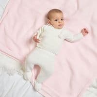 Baby lying on a pink blanket wearing a white wrap cardigan and matching footed leggings.