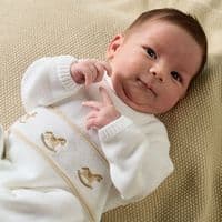 Close-up of a baby wearing the white knitted onesie with rocking horse details across the front.