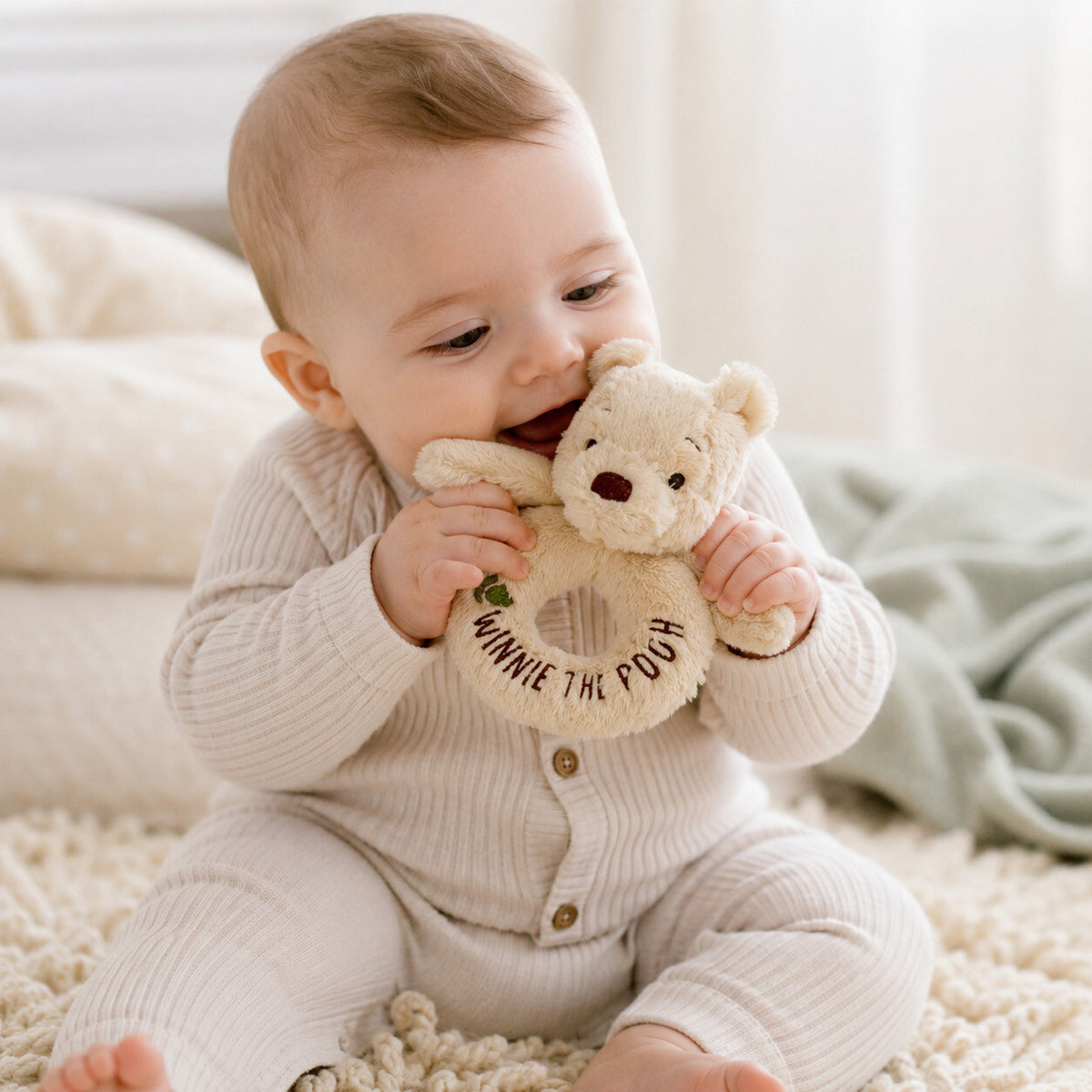 Winnie the Pooh baby rattle soft toy. This cream ring rattle is being played with by a baby