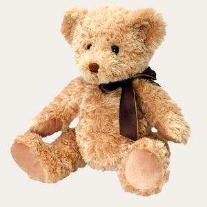 Teddy bear in a classic style, soft tan. This toy bear is sitting wearing a brown ribbon.