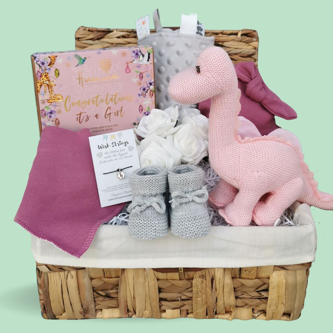 Baby girl gifts in a hamper basket. With pink dinosaur toy, taggie blanket, chocolates, booties and hat. 