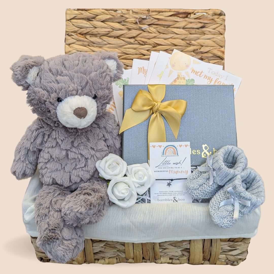 Baby shower gifts basket with chocolates, milestone cards and teddy bear in a wicker hamper.