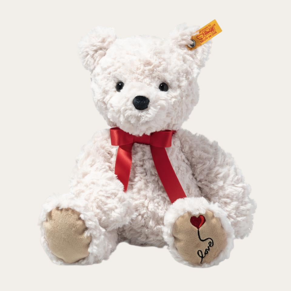 A cream-coloured teddy bear with 'Love' embroidered on the foot, wearing a red bow tie, sitting upright.