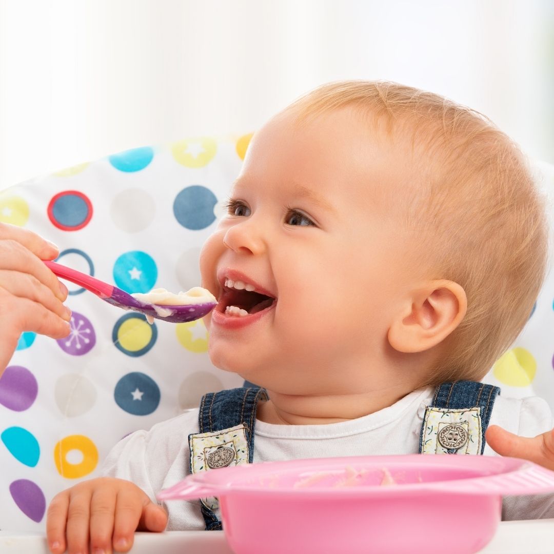 Happy baby being fed with a spoon.