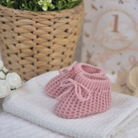 Dusty pink knit newborn baby booties with tie fastening. 