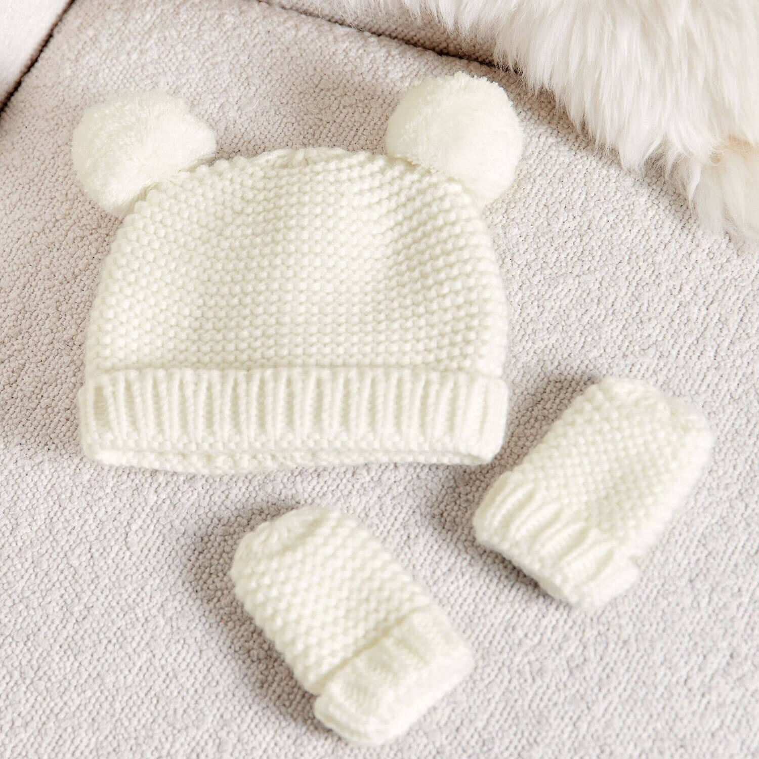 Katie Loxton White knitted baby hat and booties on a soft surface