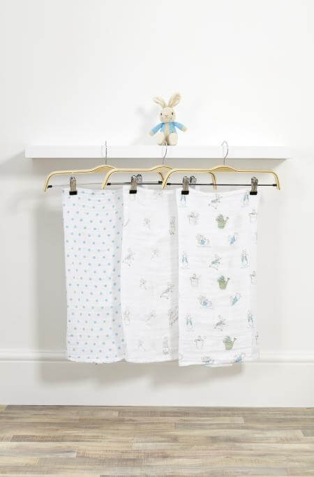 Three baby blankets with different patterns hanging on a rack against a white wall.