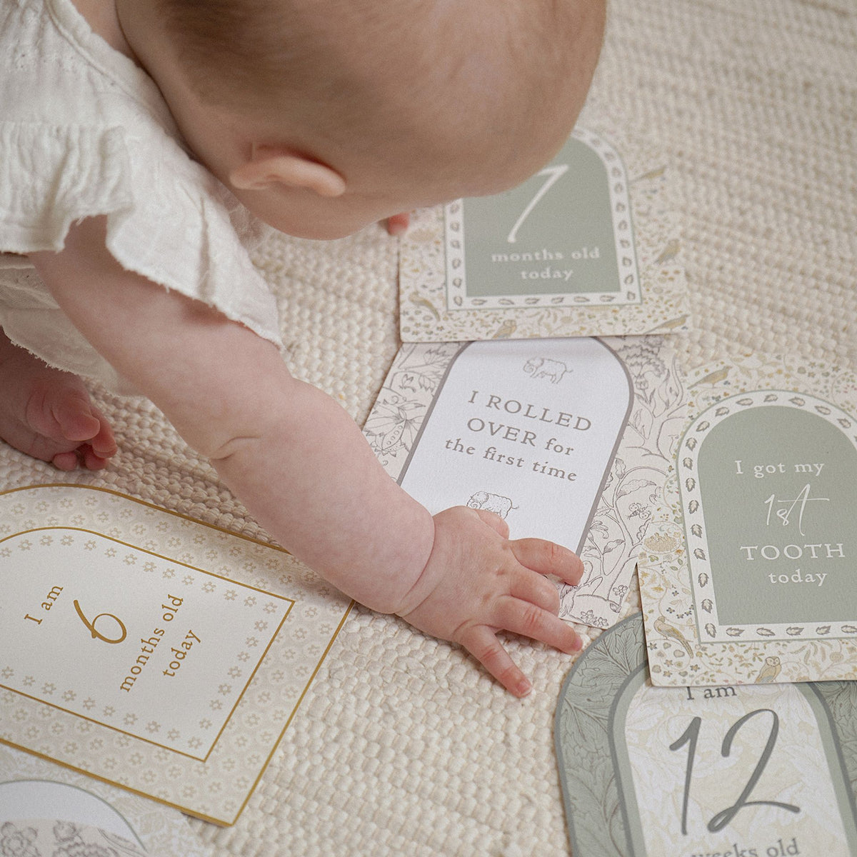 Baby reaching across arched milestone cards including rolled over and first tooth designs