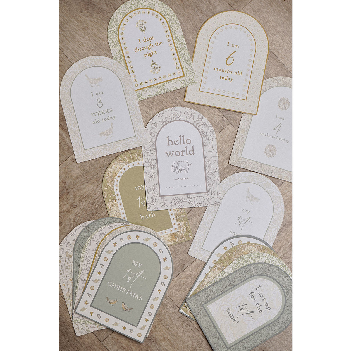 Floral milestone cards spread across a wooden surface with weeks and months visible